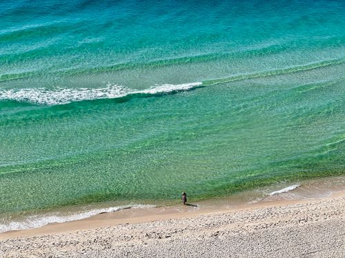 Free A peaceful beach scene with turquoise waters and a solitary person walking along the shore. Stock Photo