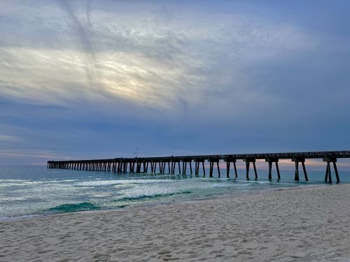Free A tranquil beach scene with a long pier extending into the ocean at twilight, under a calming sky. Stock Photo