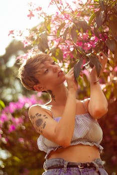 A fashionable woman with tattoos enjoys blossoms in a sunny garden setting.