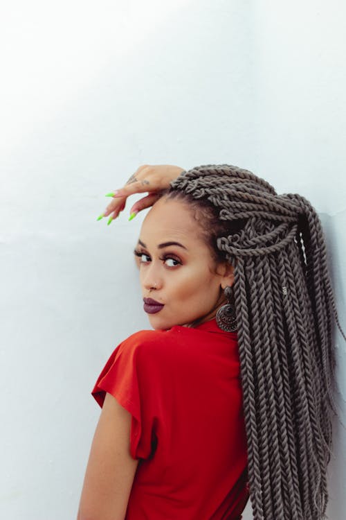 Mujer En Top Rojo Con Cabello Trenzado Apoyado En La Pared Blanca