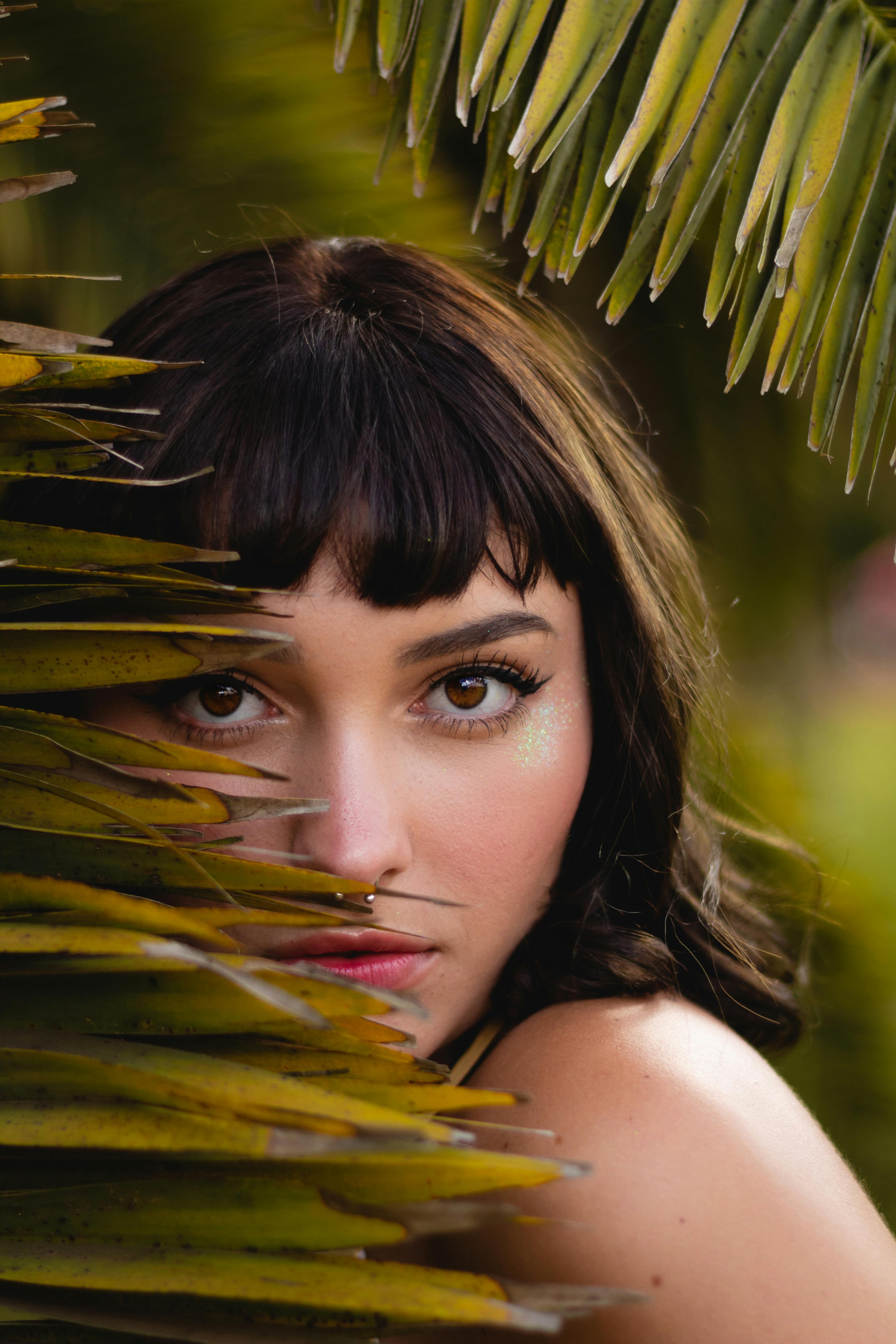 热带棕榈叶环绕着一位女士的特写肖像，营造出神秘而自然的氛围