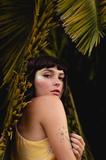 Charming portrait of a tattooed woman posing gracefully among tropical palm leaves.