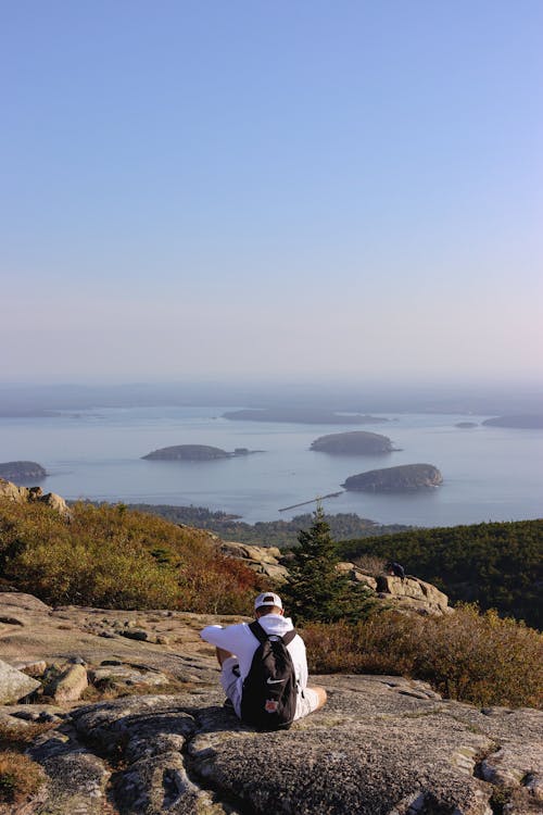 Back View of a Man with a Backpack Sitting on a Hill overlooking the Frenchman Bay in Maine, USA
