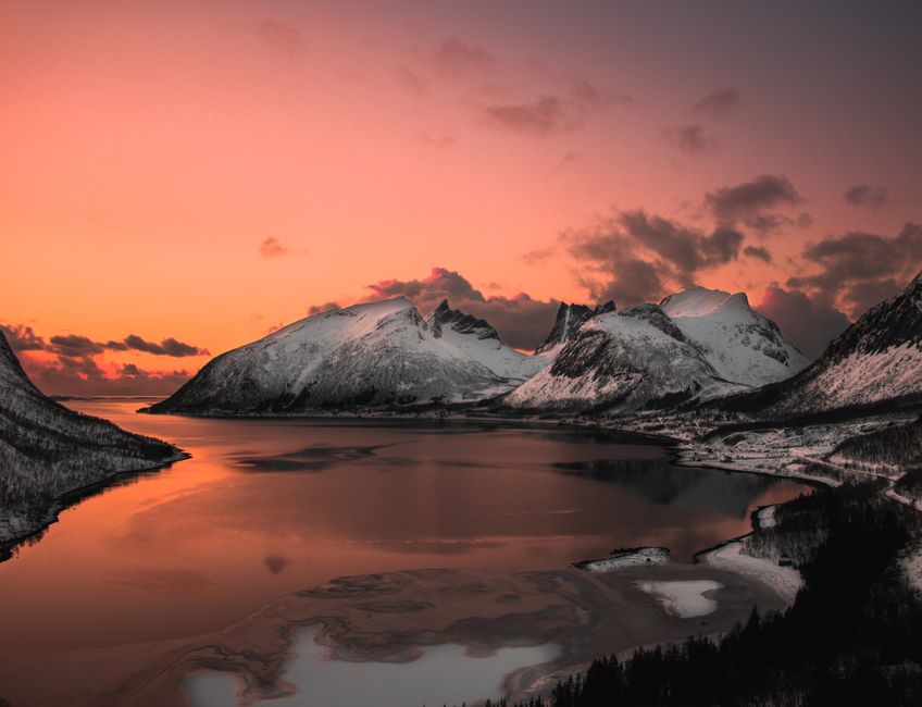 Stunning winter landscape with snowcapped mountains reflecting in a calm lake during a vibrant sunset.
