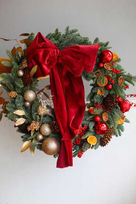 Cheerful holiday wreath adorned with red bow, pine cones, and ornaments.