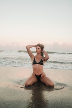 Model posing in a bikini on a serene beach at sunset.