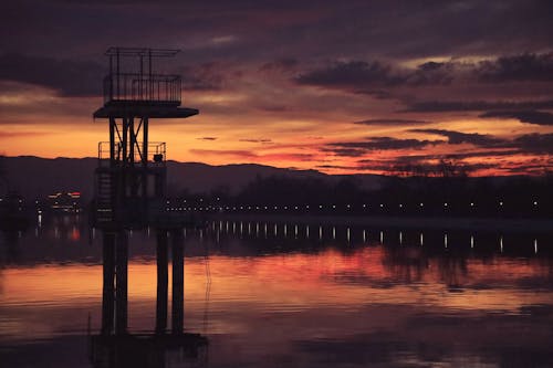 Silhouetted Tower in a Body of Water Surrounded with Trees and Hills at Sunset 