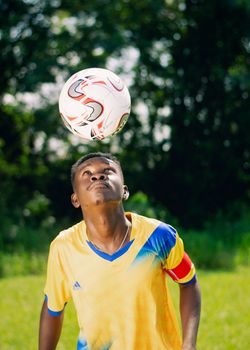 A young man skillfully balances a soccer ball on his head in a sunny outdoor setting.