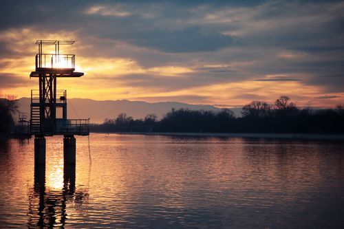 Free Silhouette of a diving platform at sunset reflecting over a tranquil lake. Stock Photo