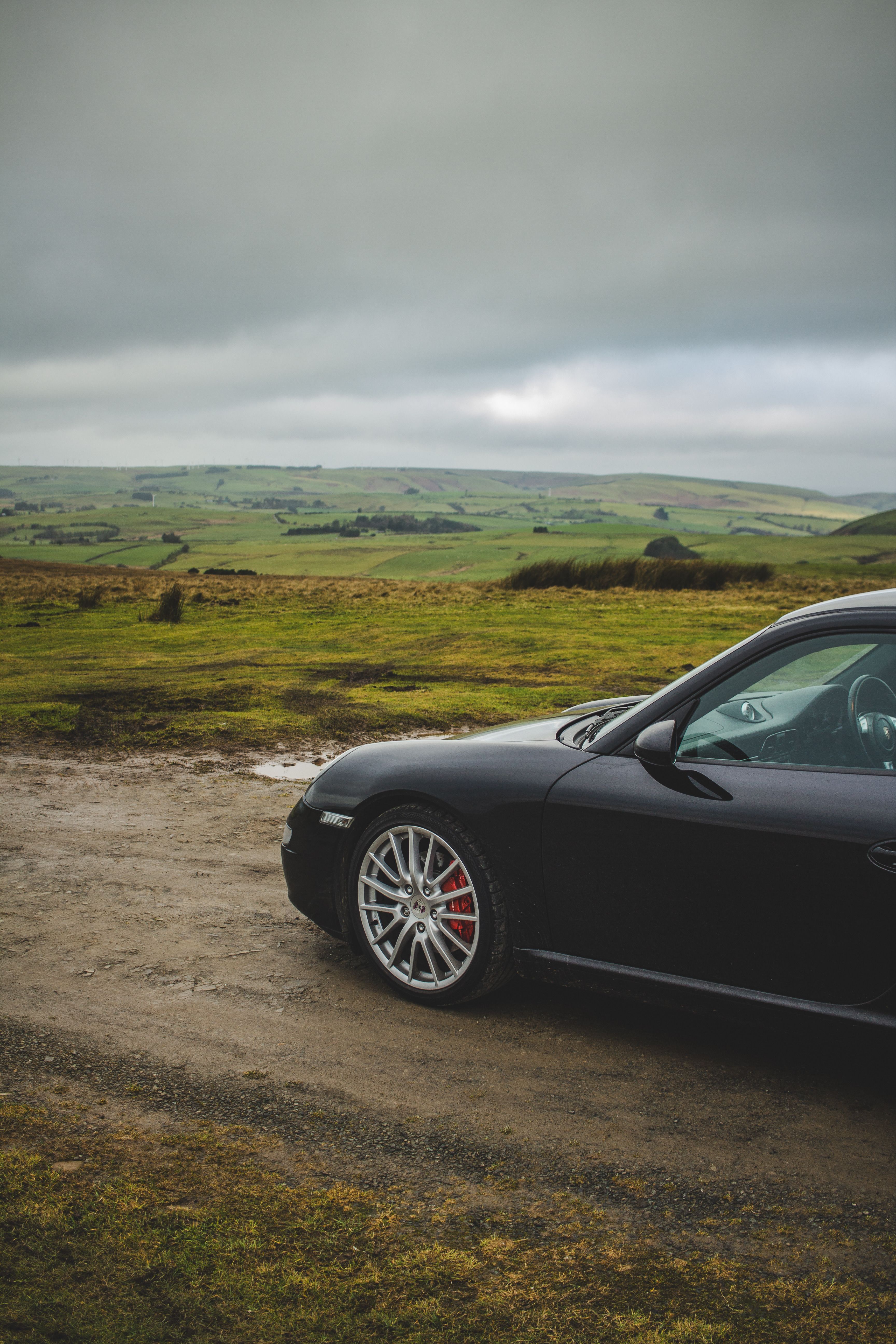 Black luxury car parked on a rural dirt road overlooking a scenic green landscape.