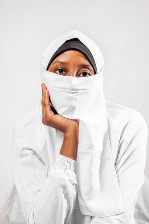Free A young woman wearing a white niqab poses for a studio portrait against a white background. Stock Photo