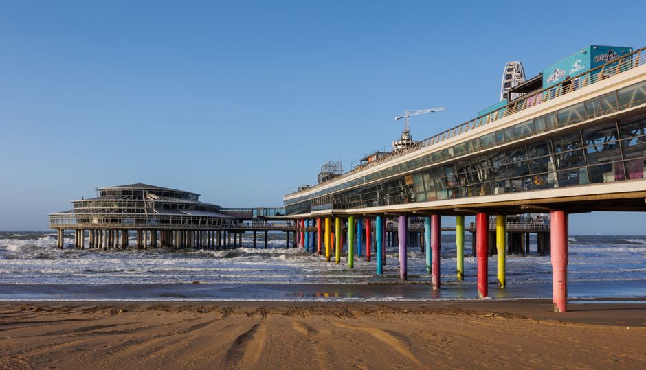 Vibrant pier stretching over the sandy beach at Scheveningen, The Hague, on a sunny day.