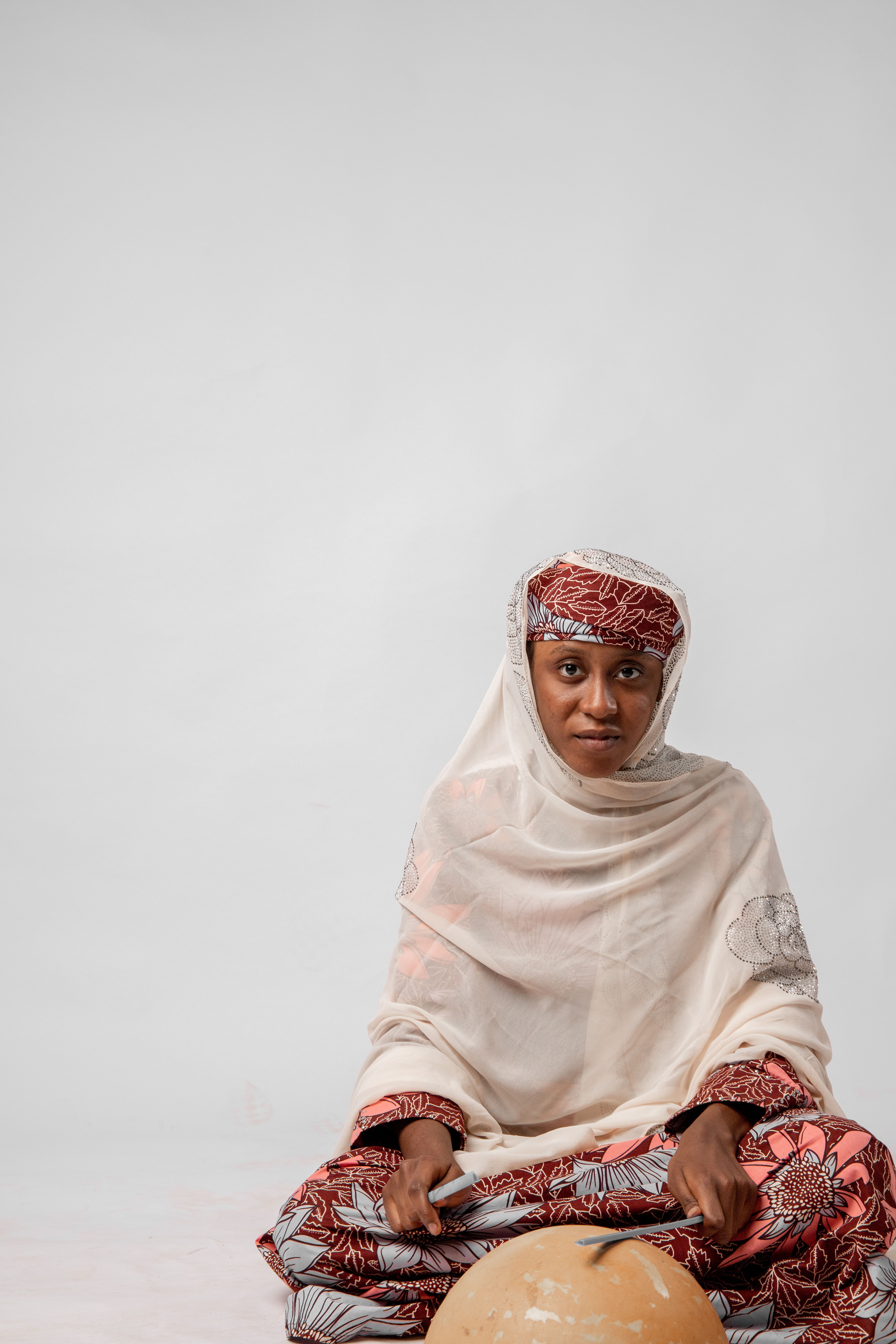 Studio portrait of a woman in colorful traditional attire and hijab on a white background.