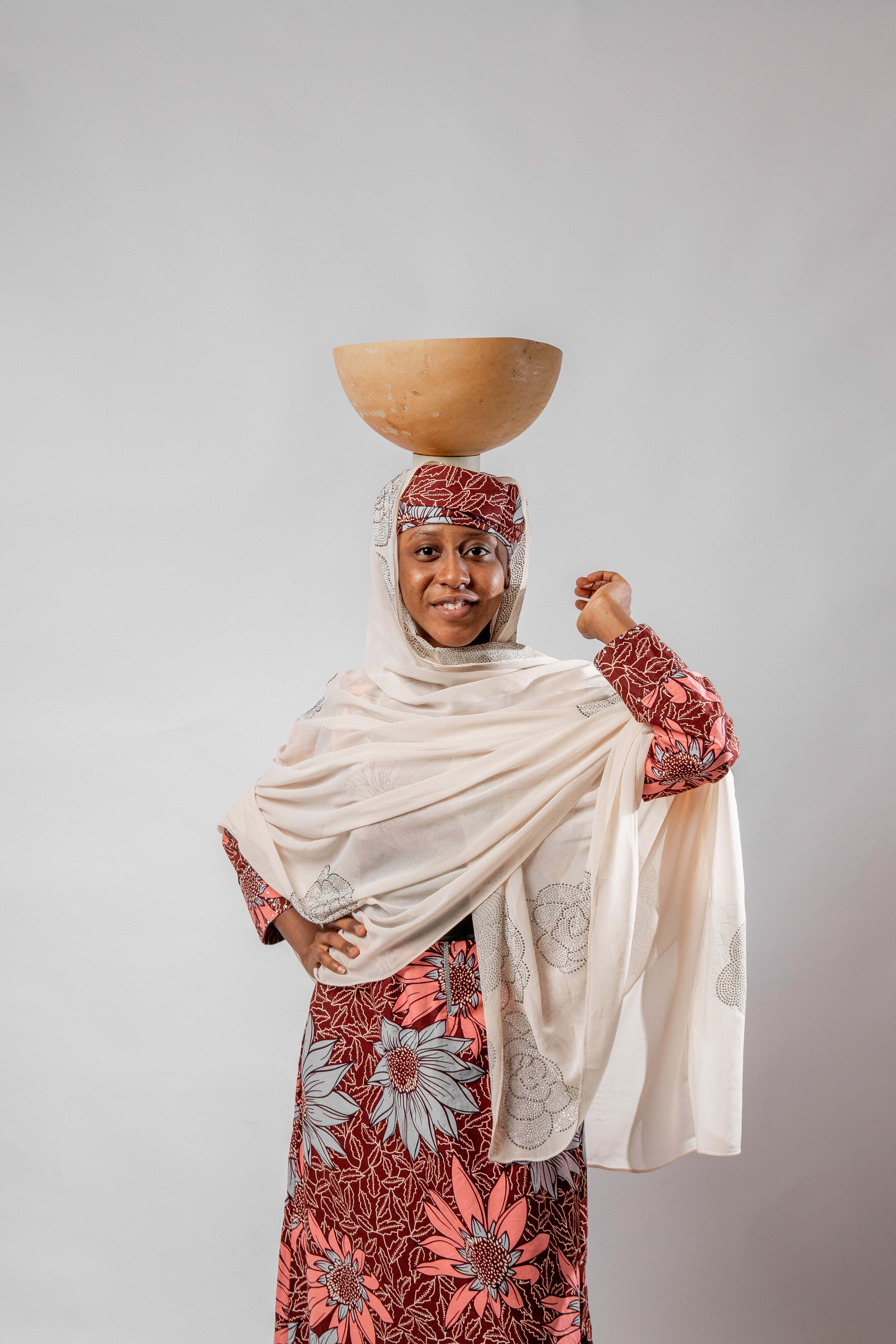 Woman in traditional attire balancing a bowl on her head, studio portrait.
