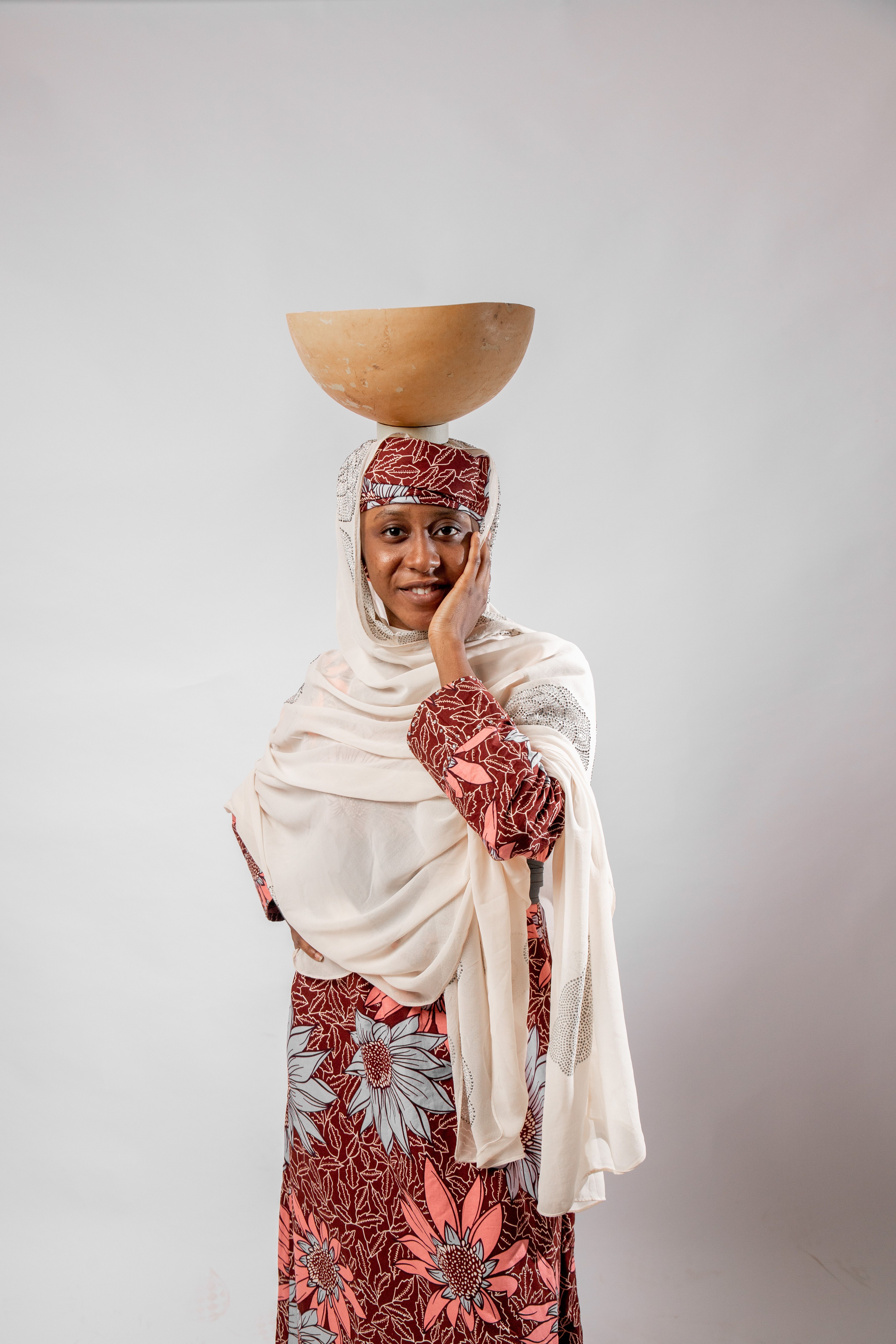 Portrait of an African woman in traditional dress balancing a bowl on her head, embodying cultural grace.
