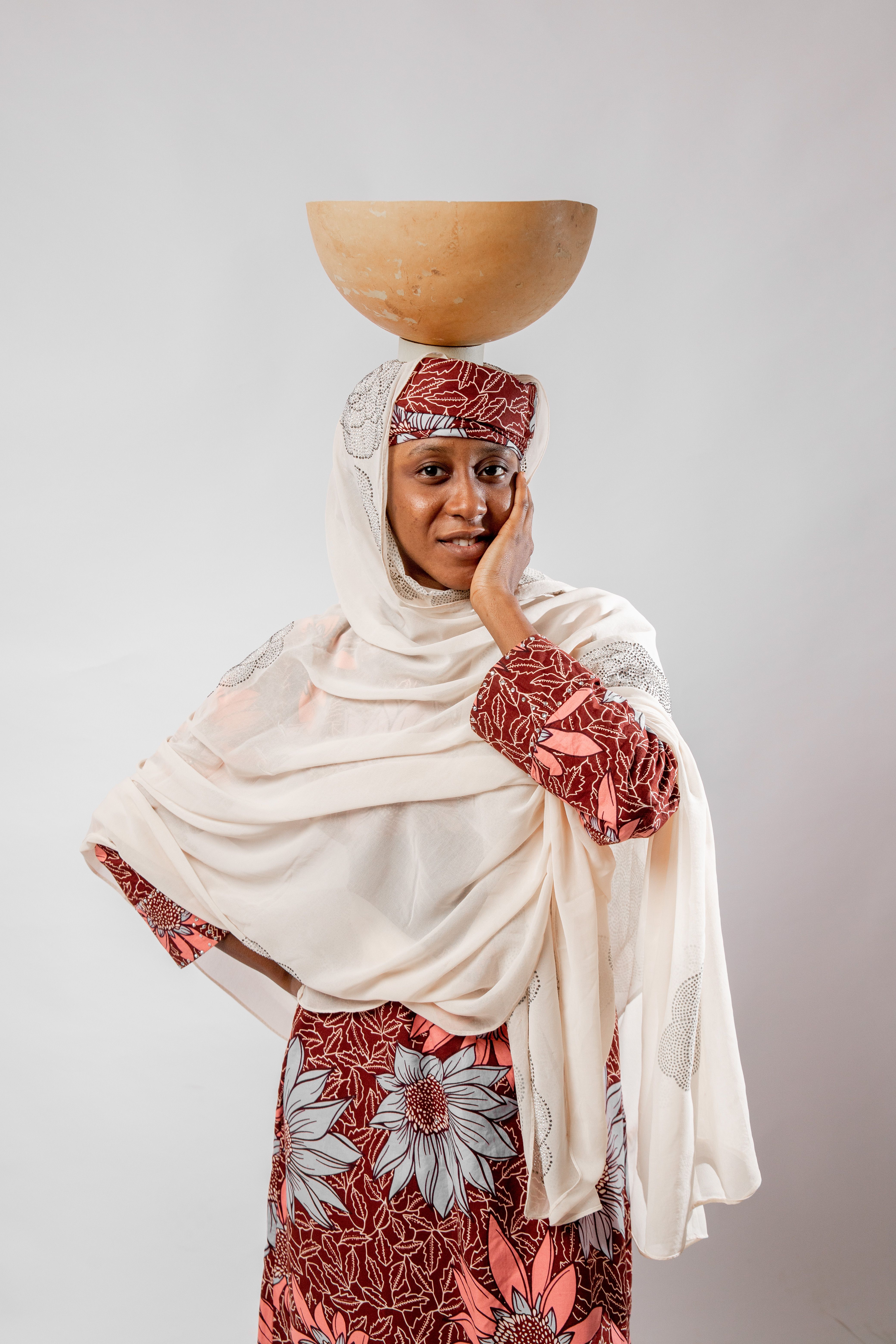 Portrait of a woman in traditional attire balancing a bowl on her head in a studio setting.