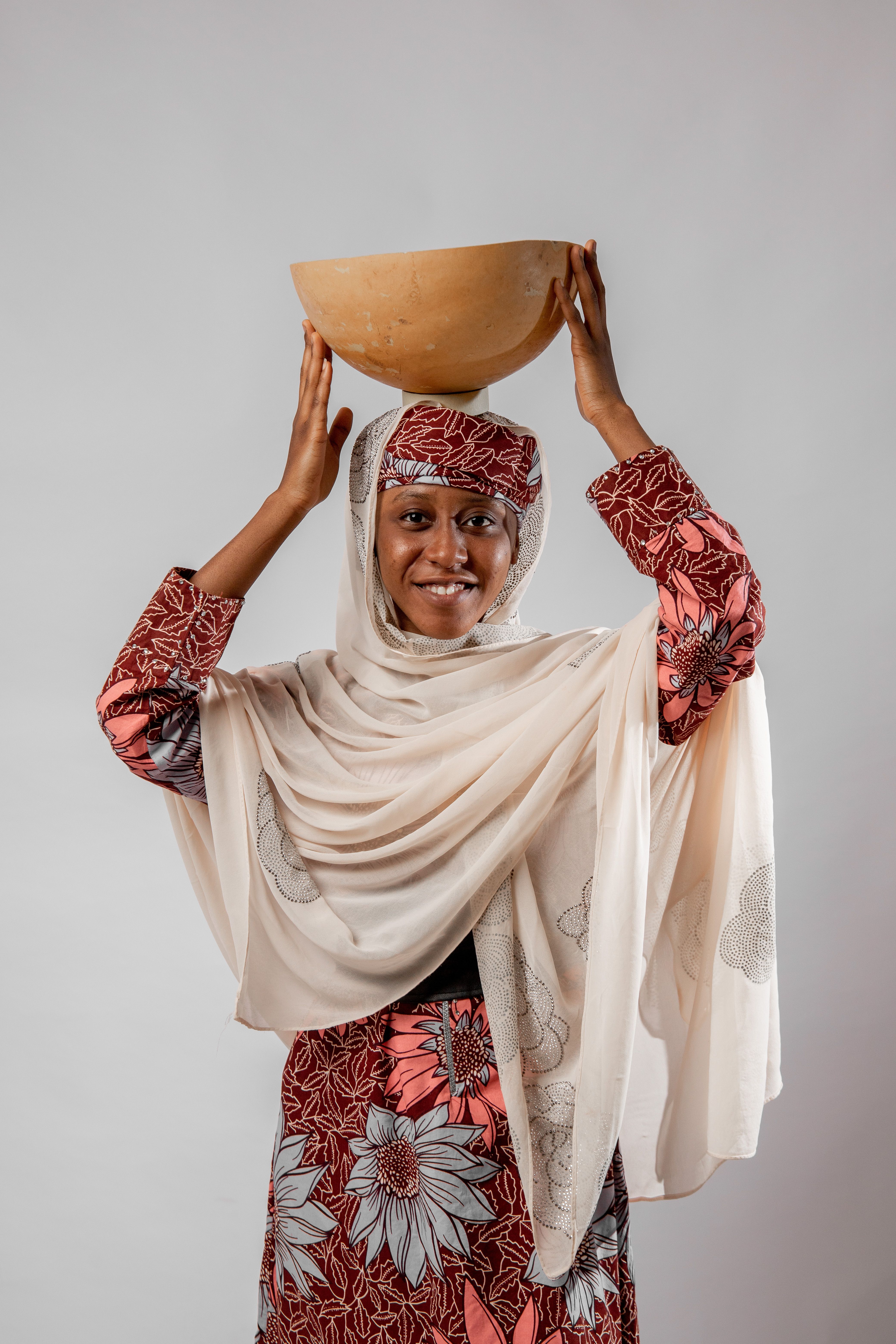 Smiling African woman in traditional clothing holding a wooden bowl indoors.