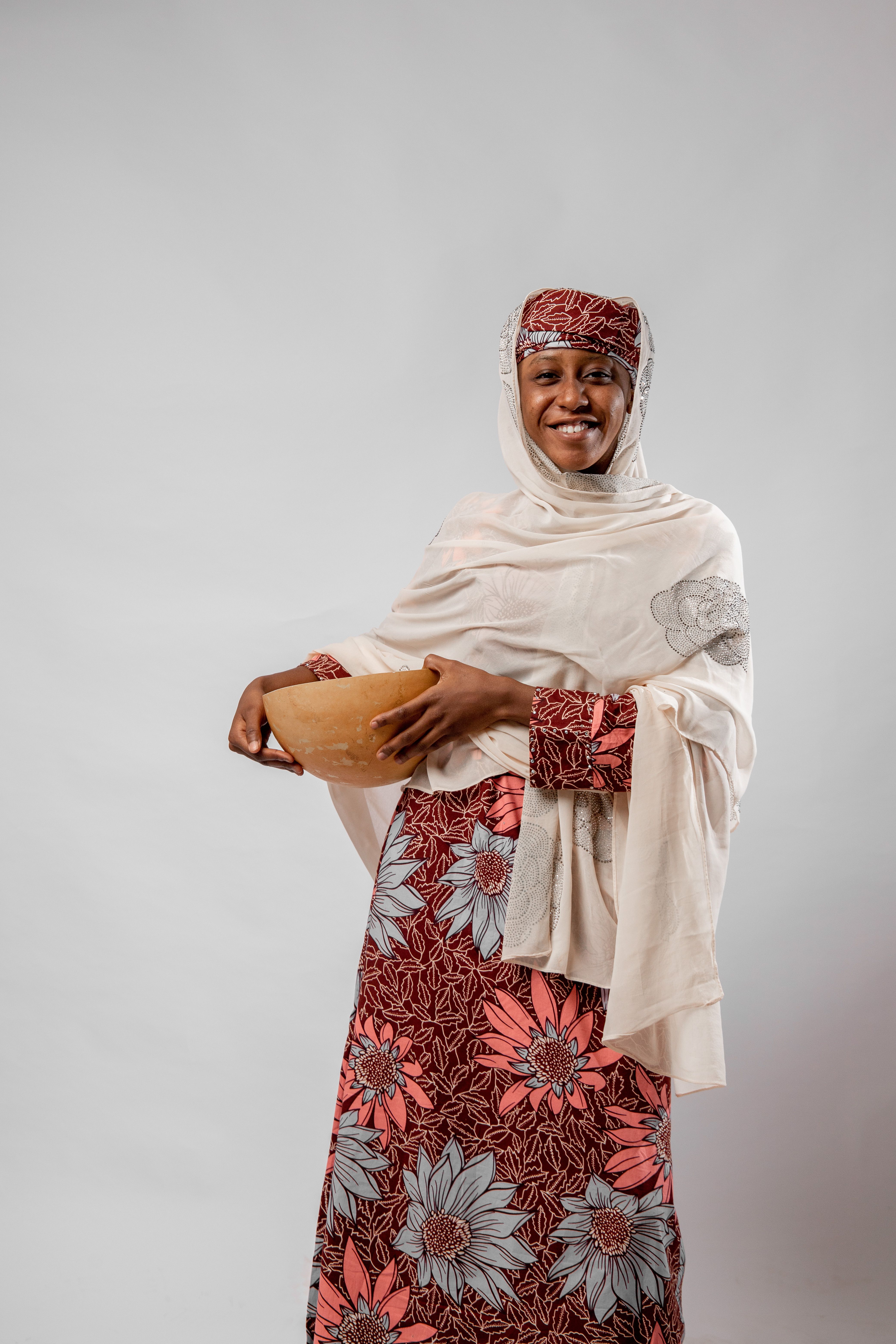 Smiling African woman in colorful traditional attire holding a wooden bowl indoors.