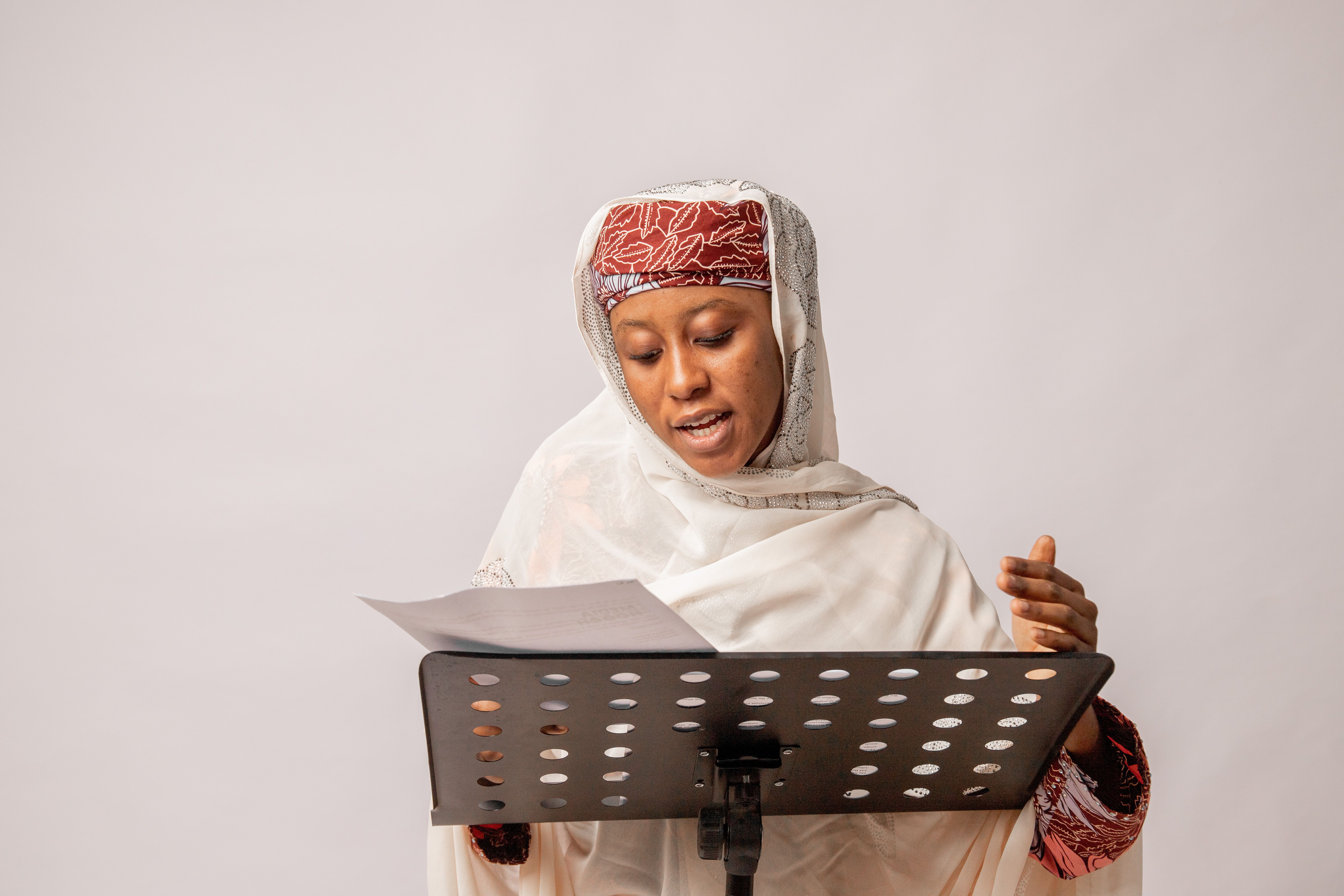 African woman wearing scarf singing in a studio, focusing on her performance.