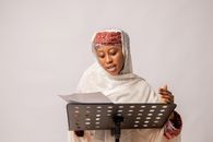 African woman wearing scarf singing in a studio, focusing on her performance.