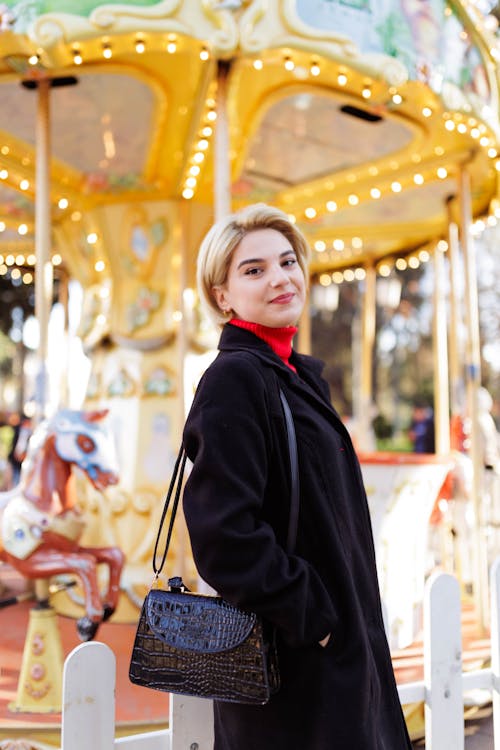 Free A woman in a black coat and black purse standing next to a carousel Stock Photo