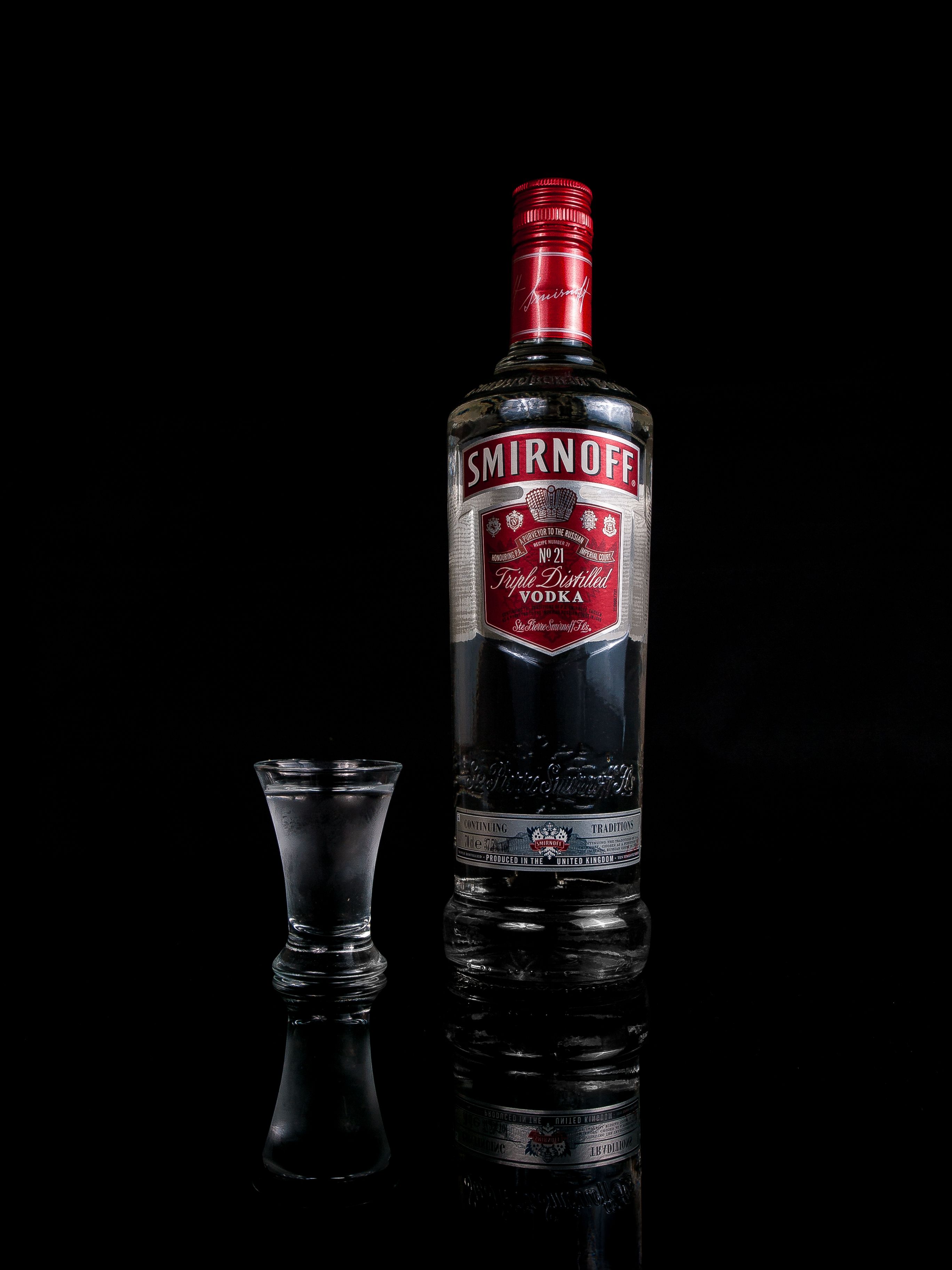 Close-up of Smirnoff vodka bottle and shot glass isolated against a black backdrop.