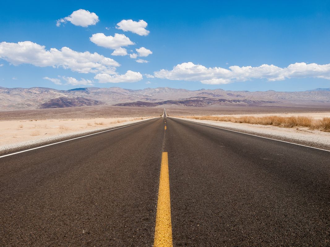 A long straight road running toward distant mountains - One Book, One Author, One Story