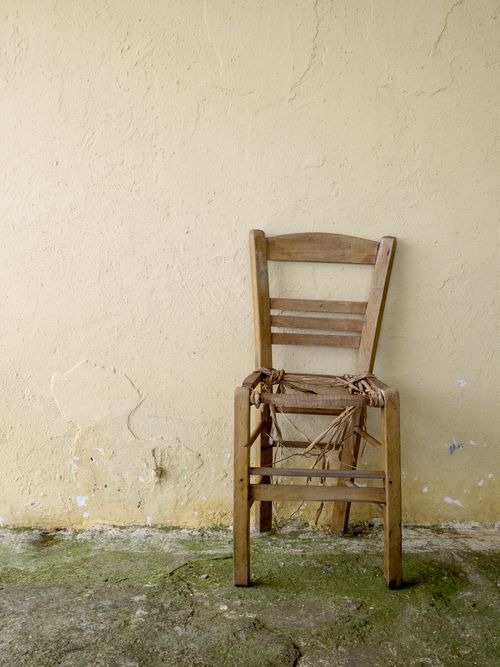 Free Old wooden chair against a cracked wall, showcasing rustic charm and decay. Stock Photo