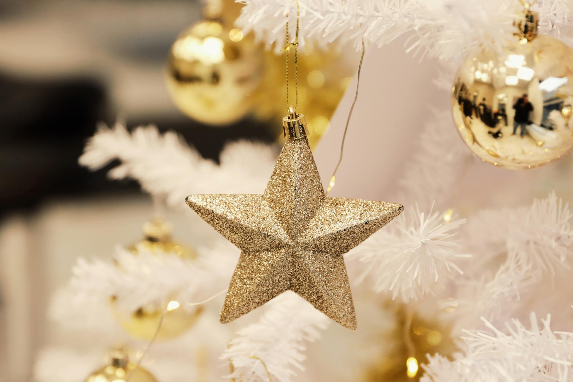 A shimmering gold star and baubles enhance a white Christmas tree, creating a festive atmosphere.