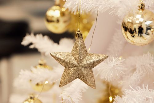 Free A shimmering gold star and baubles enhance a white Christmas tree, creating a festive atmosphere. Stock Photo