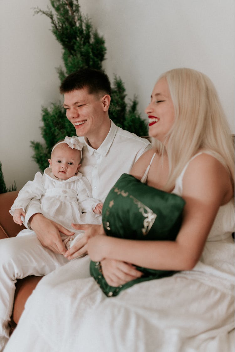 Young Family With A Baby Sitting Next To A Christmas Tree And Smiling 