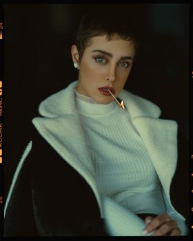 A stylish woman in a chic outfit poses with a matchstick, exuding confidence and elegance.