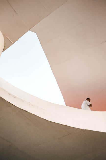 A man in a white outfit explores a modern minimalist architectural structure.