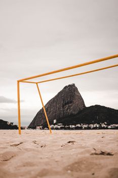 A scenic view of Sugarloaf Mountain framed by a beach soccer goal post on a sandy shore.