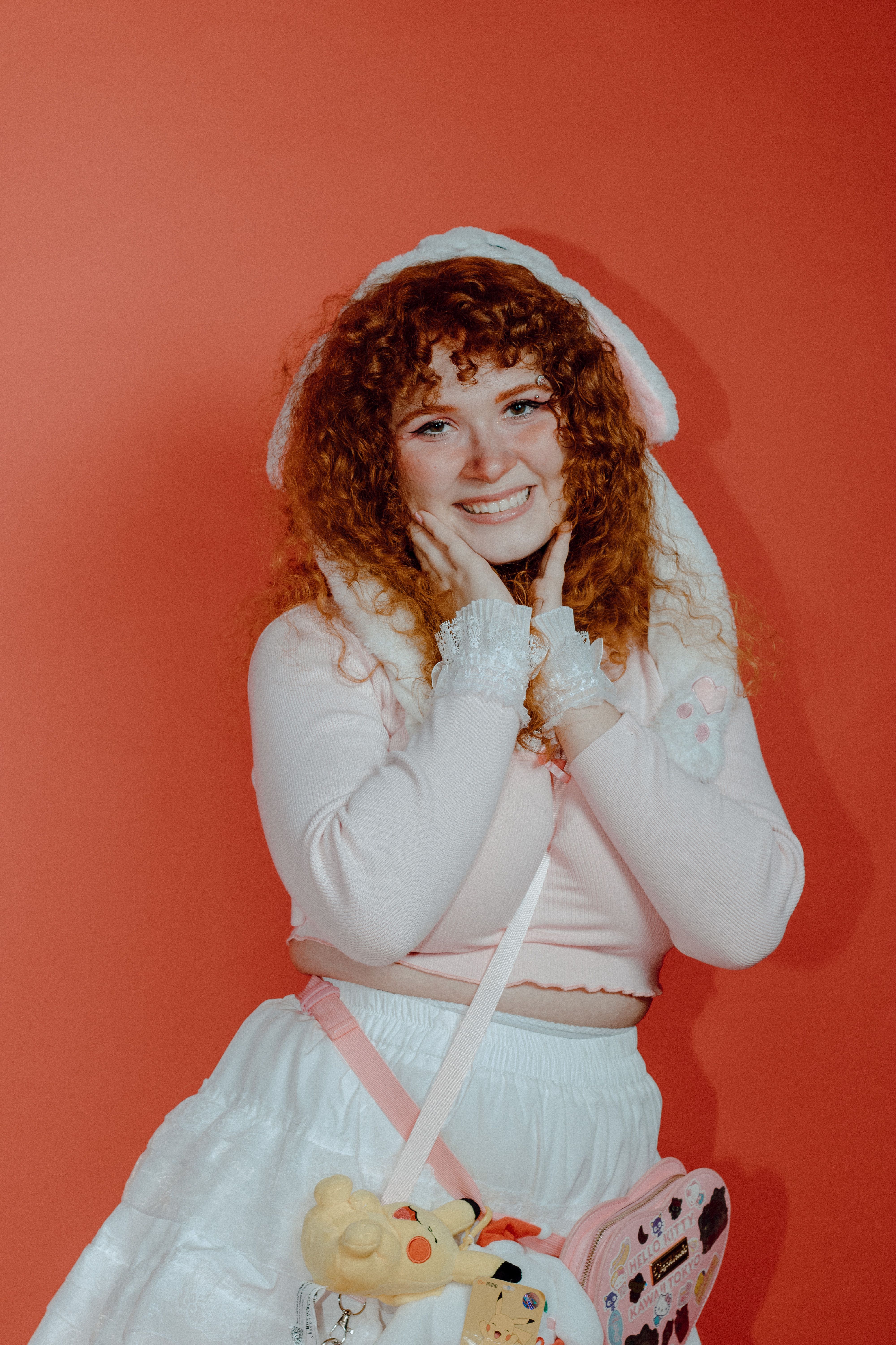 Smiling woman in white dress and red hat against a vivid background.