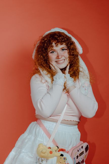 Smiling woman in white dress and red hat against a vivid background.