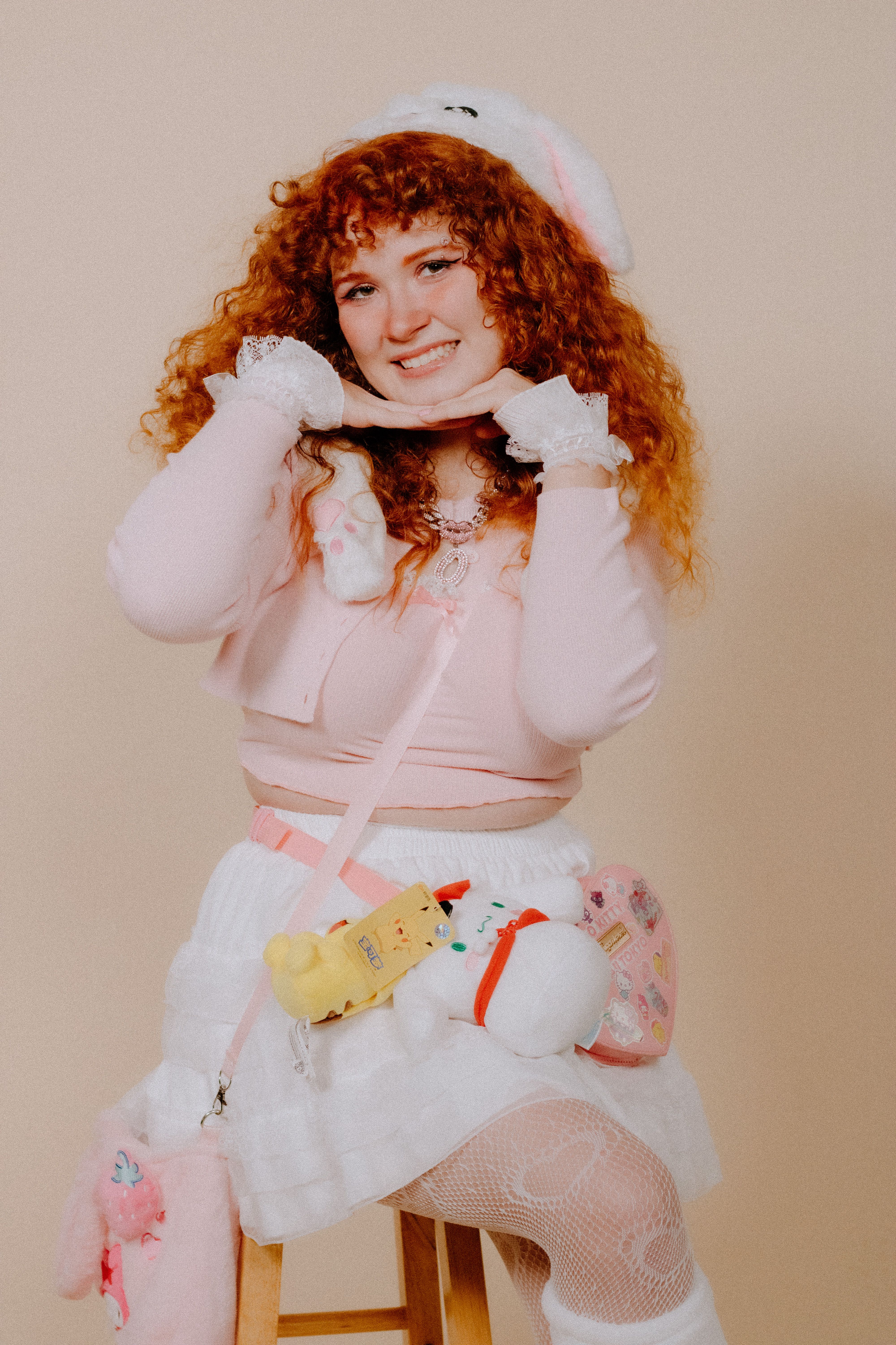Cheerful redhead in pink cosplay outfit posing with a playful smile, studio backdrop.