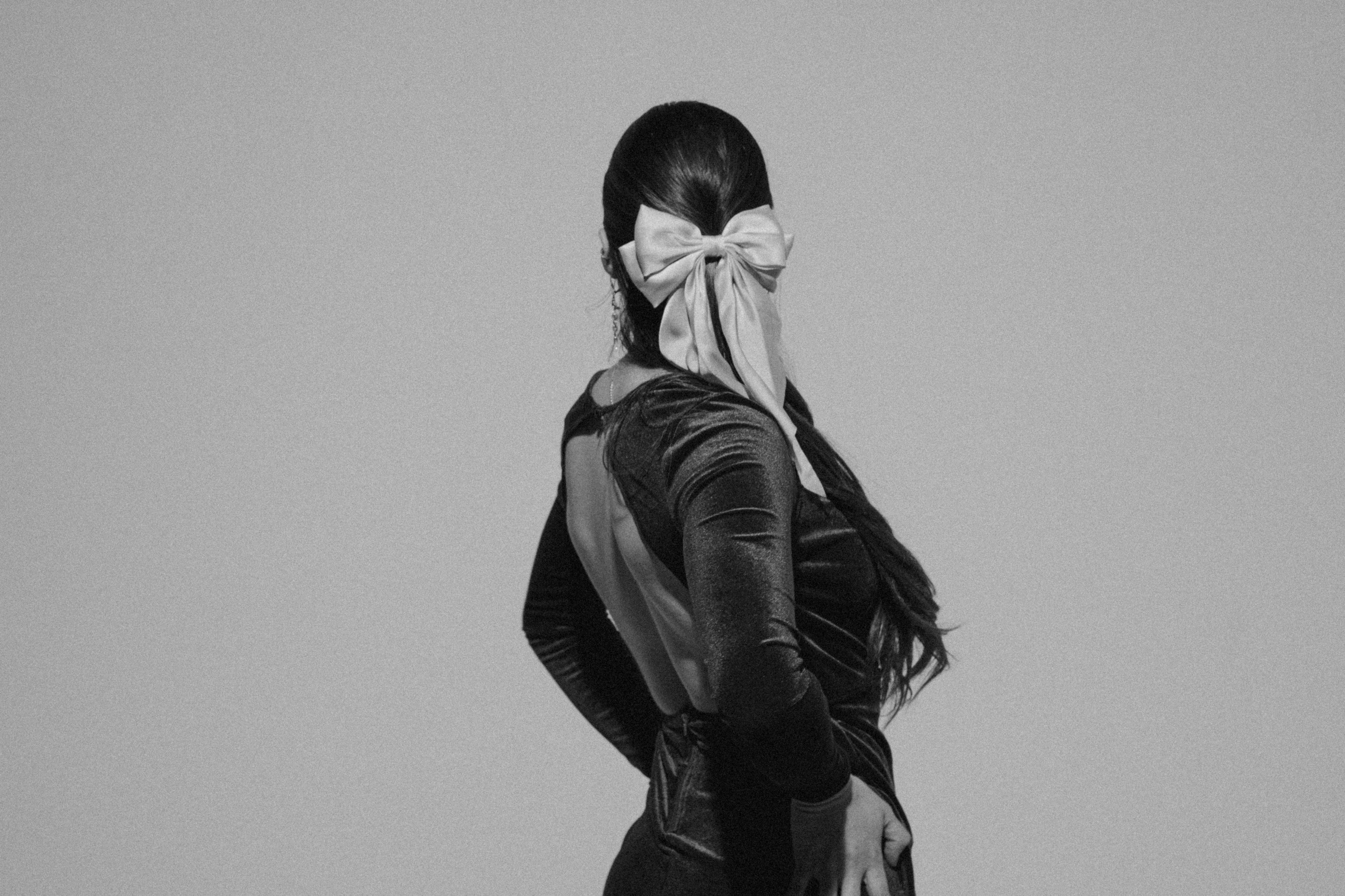 Black and white photo of a woman in a velvet dress with a bow, posing gracefully.