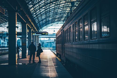Free Silhouettes of commuters waiting at a railway station platform in an urban setting. Stock Photo