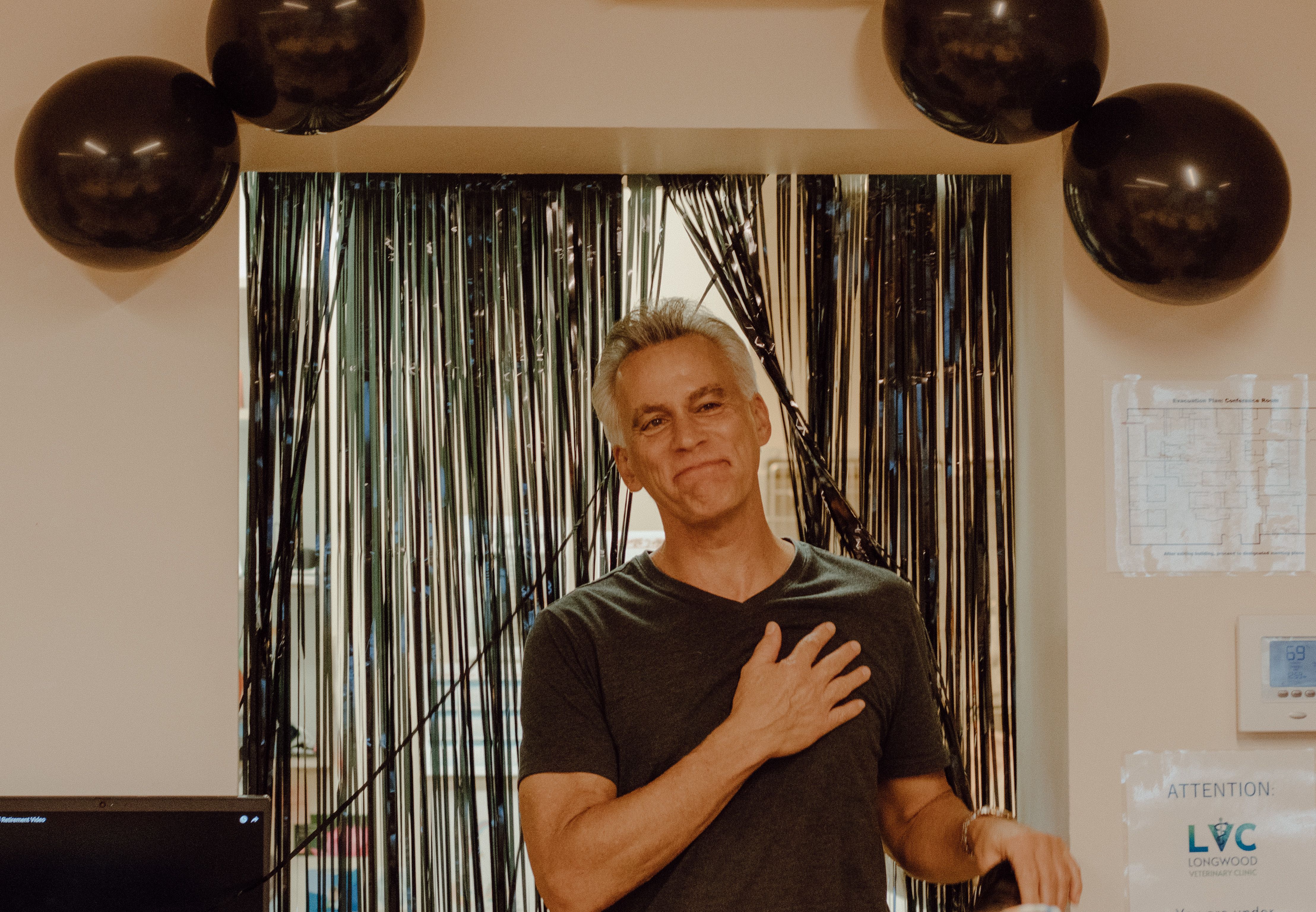 A mature man in a festive setting, smiling with gratitude during a celebration with black balloons indoors.