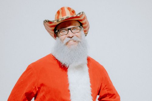 Free Man dressed as Santa Claus wearing a red striped cowboy hat, smiling against a white background. Stock Photo
