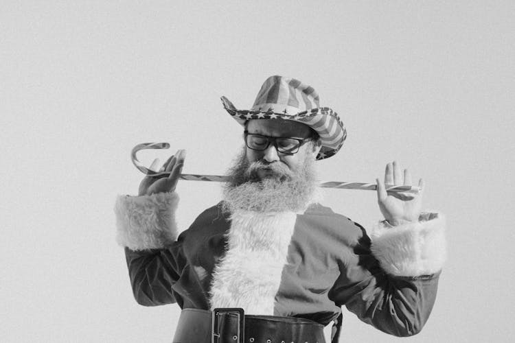 Senior Bearded Man In Santa Costume And Cowboy Hat With Cane