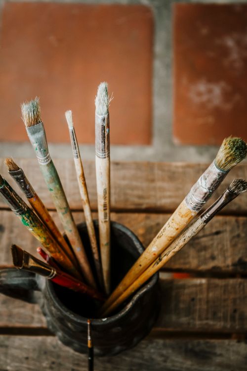 Free Artistic still life of used paintbrushes in metal cup on wooden table, warmly lit. Stock Photo