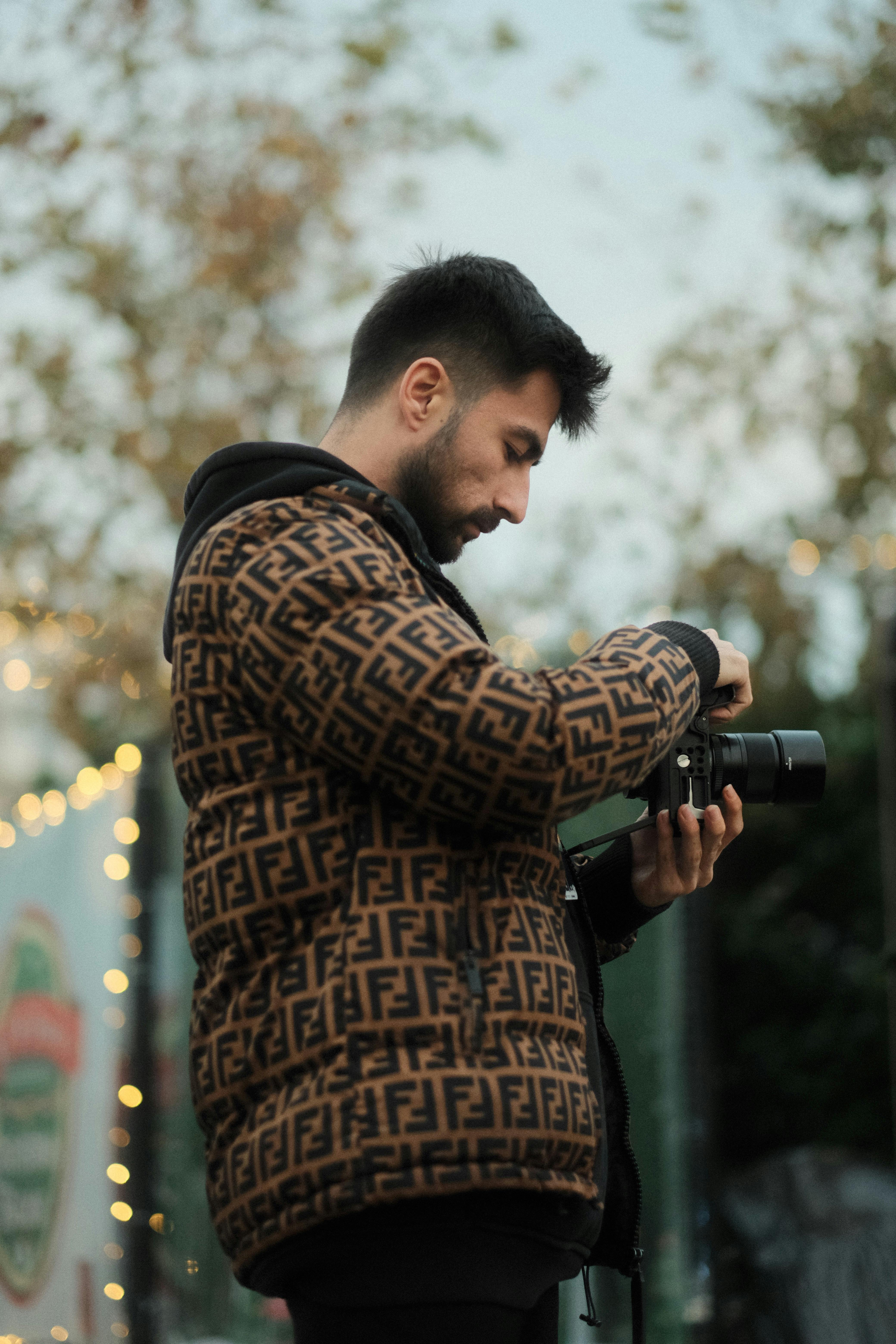 Man in patterned jacket checking camera settings outdoors during fall.
