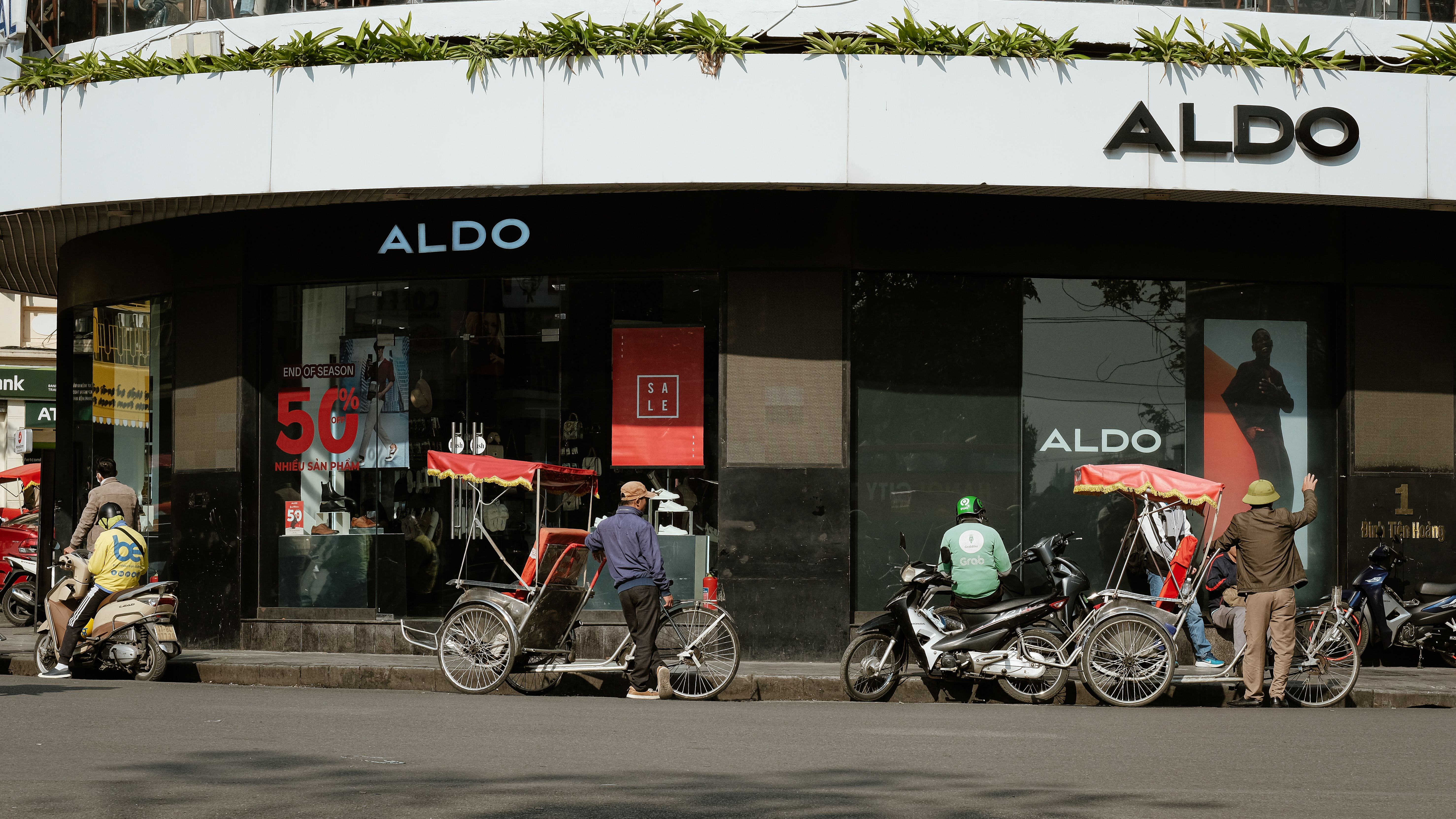 Busy city street corner with bicycles, motor scooters, and storefronts during daytime.