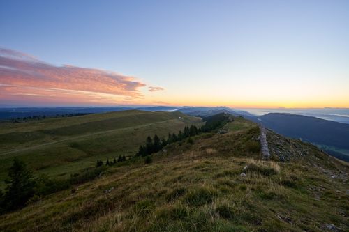 Free A breathtaking view of the Swiss Alps in summer with rolling hills and a vibrant sunset sky. Stock Photo