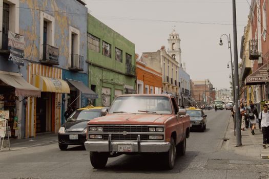 A vibrant street scene captures the essence of Heroica Puebla de Zaragoza with colorful buildings and busy traffic.