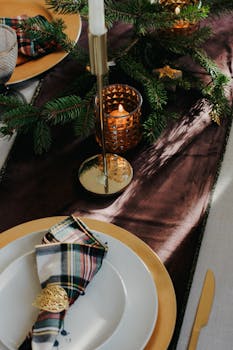 A sophisticated Christmas table setting featuring candles, evergreen branches, and plaid napkins.