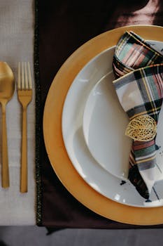 Elegant table setting featuring gold cutlery and a plaid napkin on a white plate.