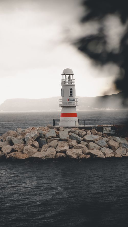 Free Scenic view of a white and red lighthouse on a rocky coastline against a moody sky. Stock Photo